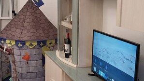 Een kamer met een speelhuis in kasteelthema, een fles wijn op een plank en een computer die een kaart toont.