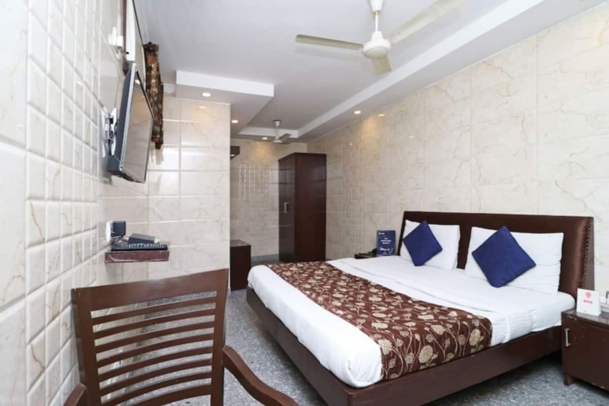 A hotel room with a bed, a desk, a chair, a TV, and a ceiling fan.