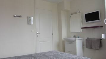 Un dormitorio con cama, una puerta blanca, televisor de pared, lavamanos y un perchero para toallas.