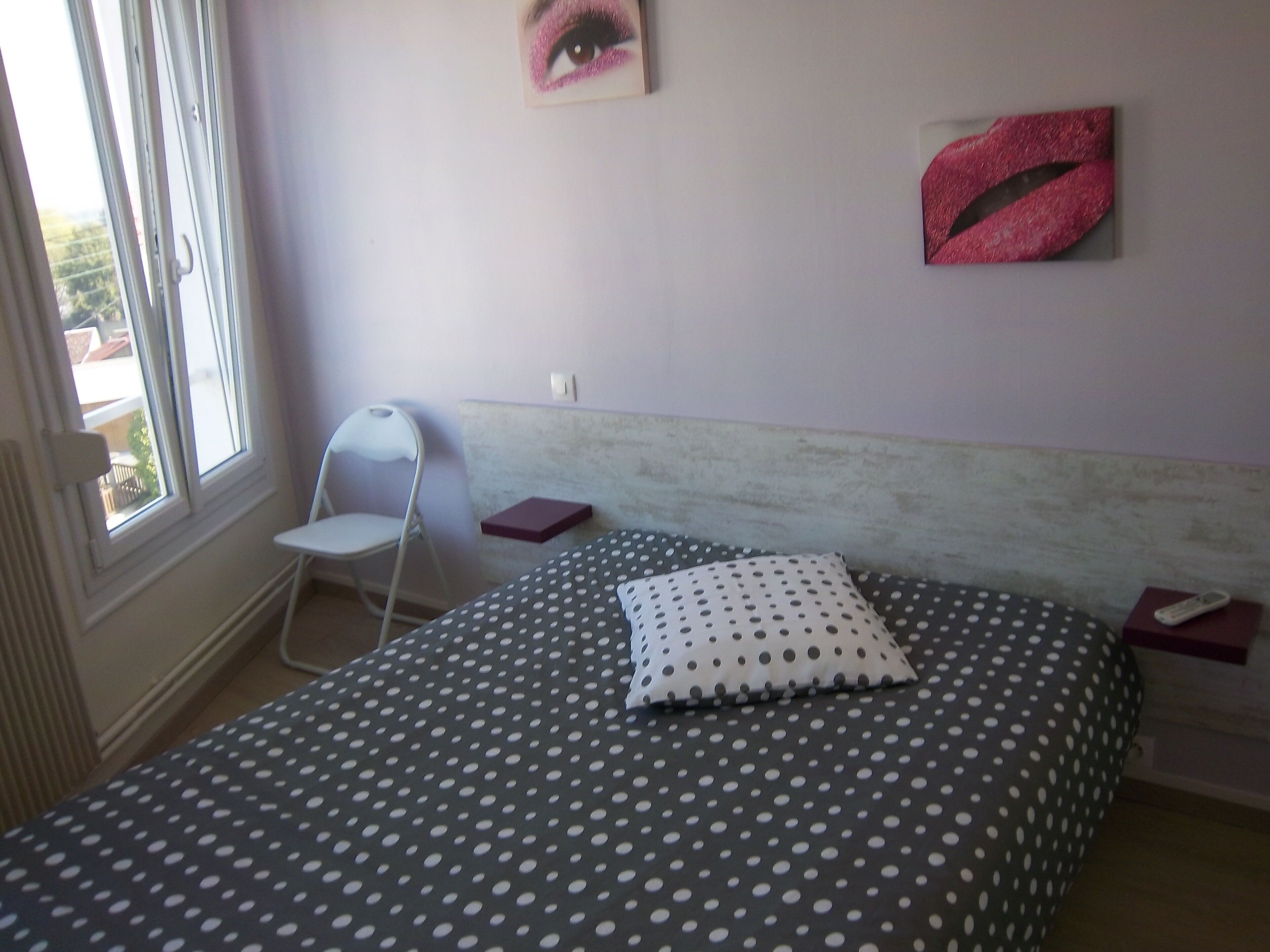 Une chambre à coucher avec un lit, une chaise, un oreiller, une décoration murale représentant des lèvres et une fenêtre.