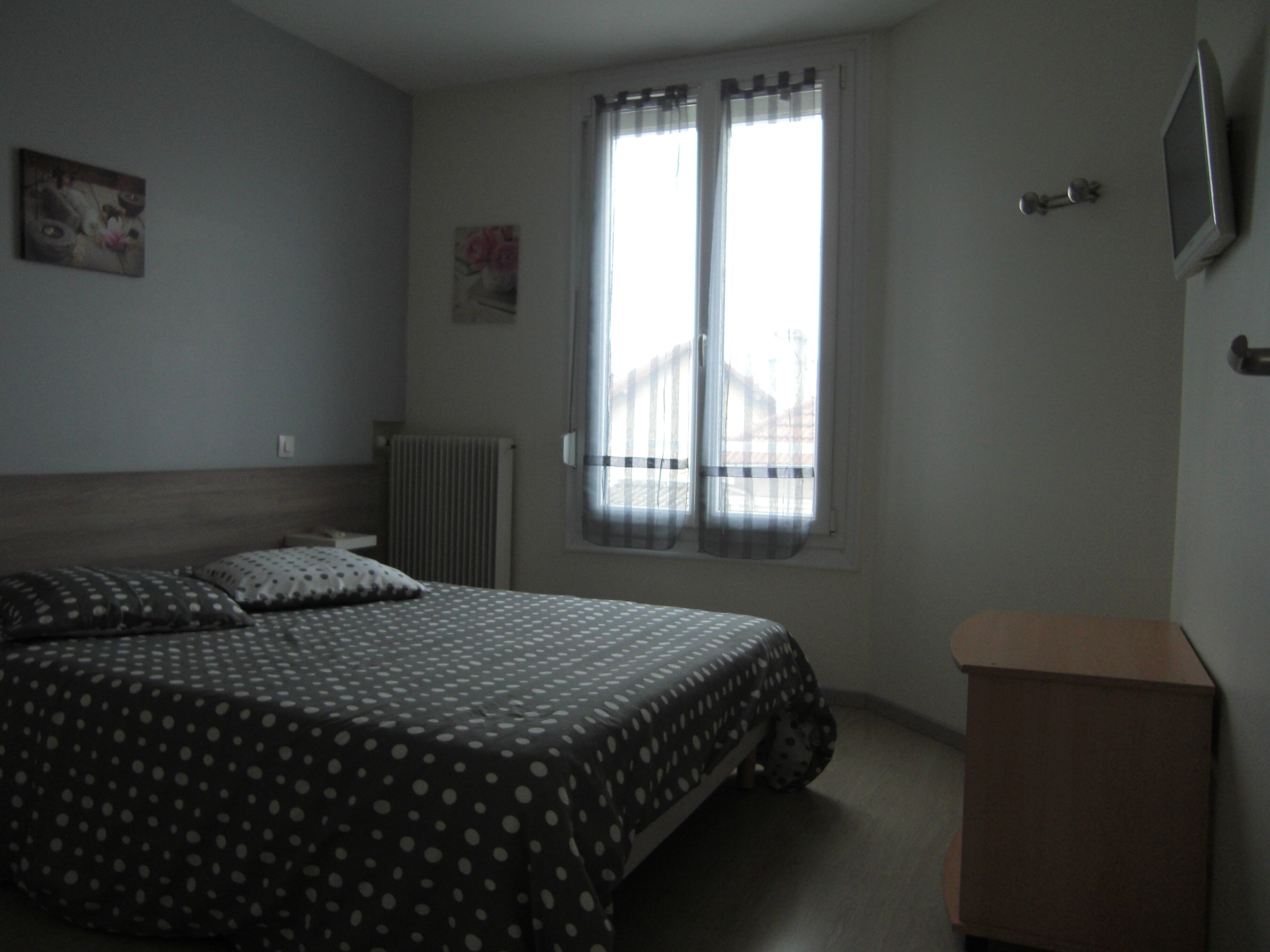 A bedroom with a bed, a radiator, a window with curtains, and a TV on the wall.