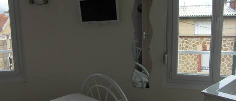 A bedroom with a bed, a TV mounted on the wall, and a window with a view of buildings.