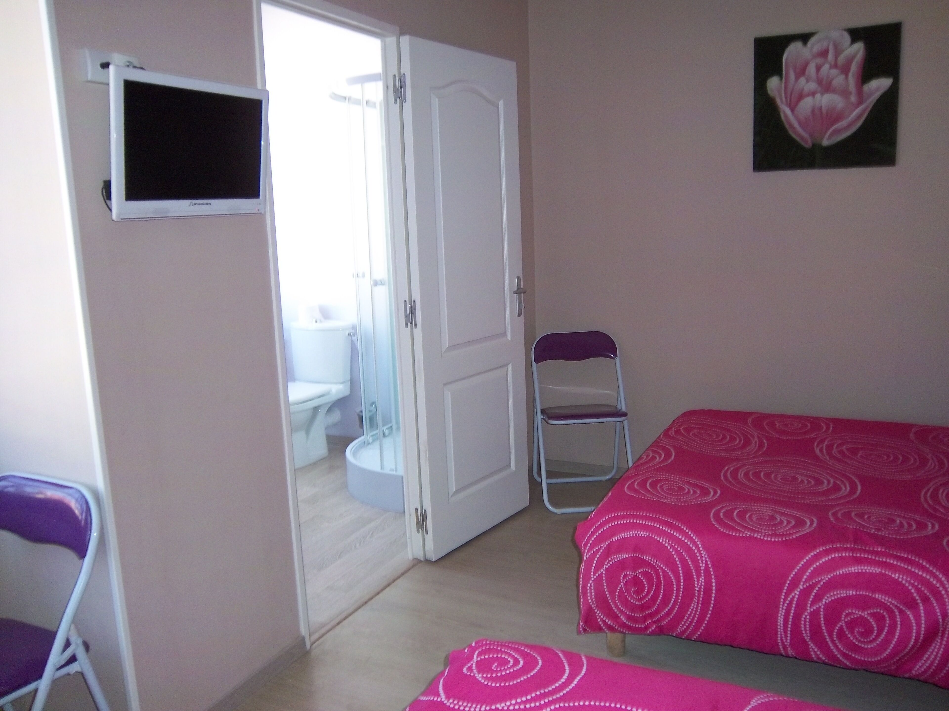 Une chambre avec deux lits, une télévision, une salle de bain visible à travers une porte ouverte et une chaise.