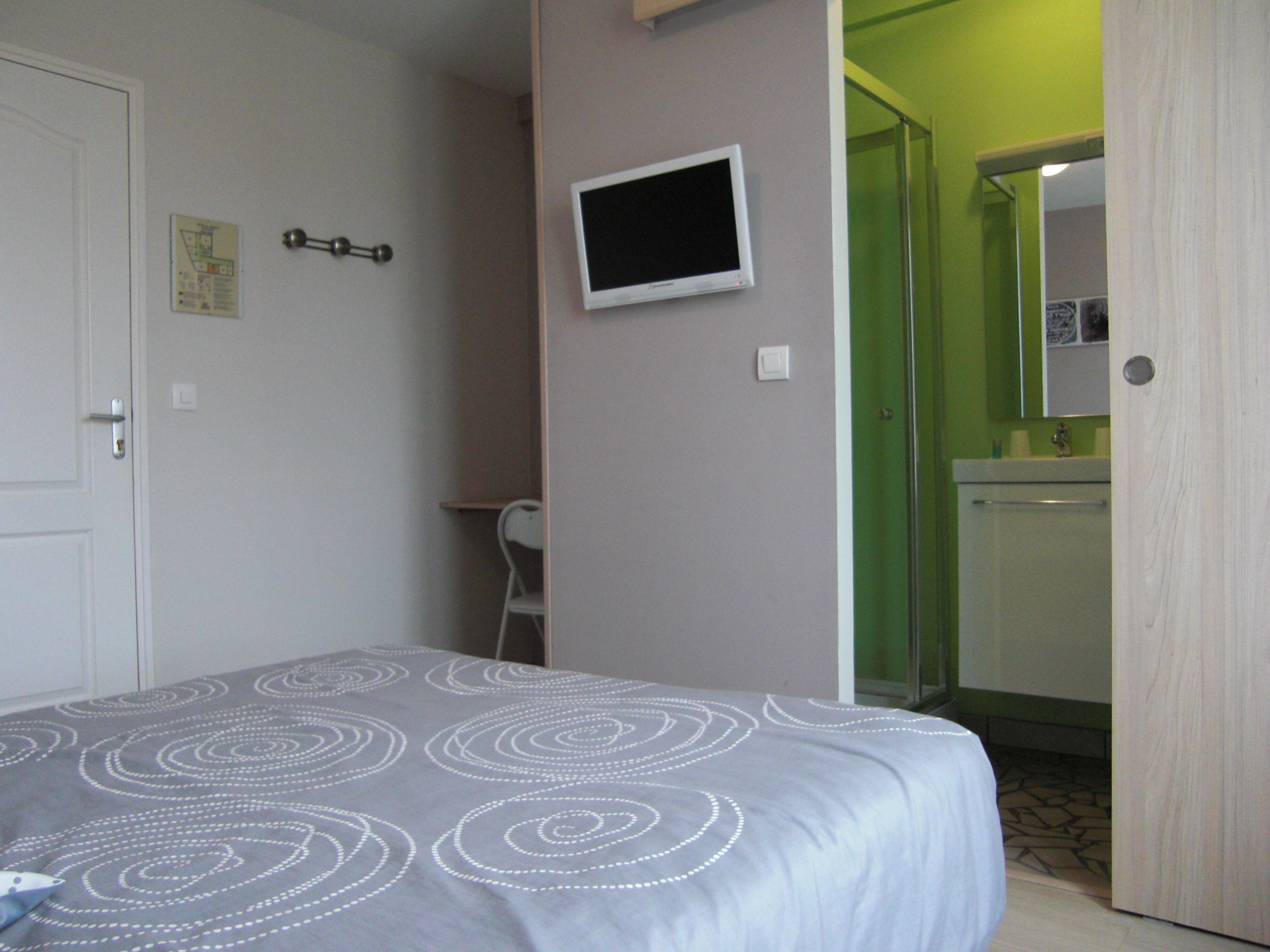 Un dormitorio con una cama, un televisor montado en la pared y un baño visible a través de una puerta abierta.