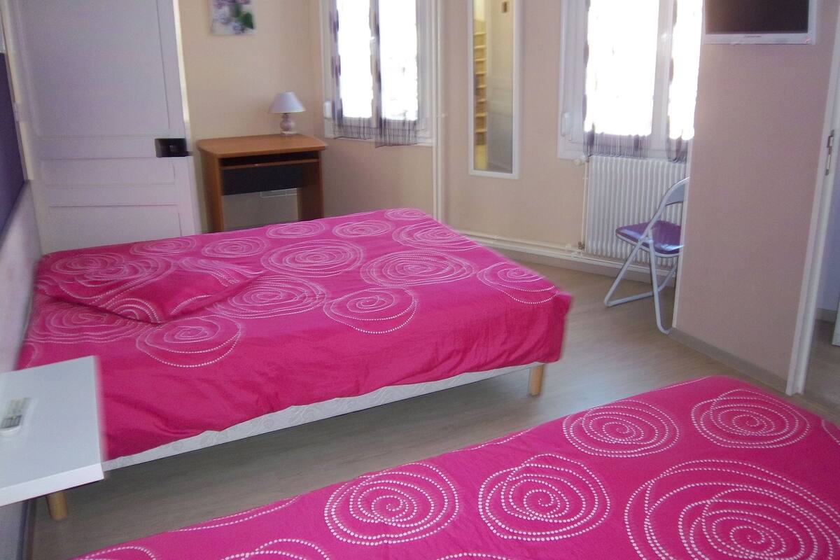A bedroom with a bed, a chair, a small table, a mirror, and a radiator.