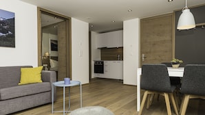 Un salon moderne avec un canapé gris, un petit pouf rond et un coin repas comprenant une table et des chaises.
