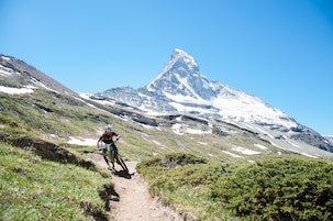 Un ciclista de montaña en un sendero de tierra, con un pico nevado al fondo.