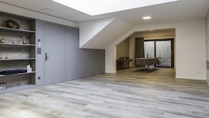 Un intérieur moderne avec une verrière, des meubles de rangement gris, un coin repas et un plancher en bois.