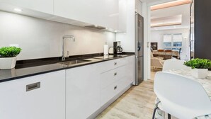 A modern kitchen with white cabinetry, a black countertop, and stainless steel appliances. There is a dining area visible through an open doorway. - Luxurious apartment near Plaza Castilla, garage space. (Madrid)