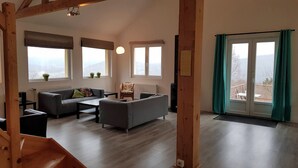 A spacious living room with a sofa, armchair, and coffee table. There are large windows with curtains, a radiator, and a view of the outdoors. - Large, light and modern holiday home, beautiful view, beautifully situated (Ban-sur-Meurthe-Clefcy)