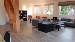 A modern living room with a staircase, a bookshelf, a sofa, and a coffee table. - Large, light and modern holiday home, beautiful view, beautifully situated (Ban-sur-Meurthe-Clefcy)