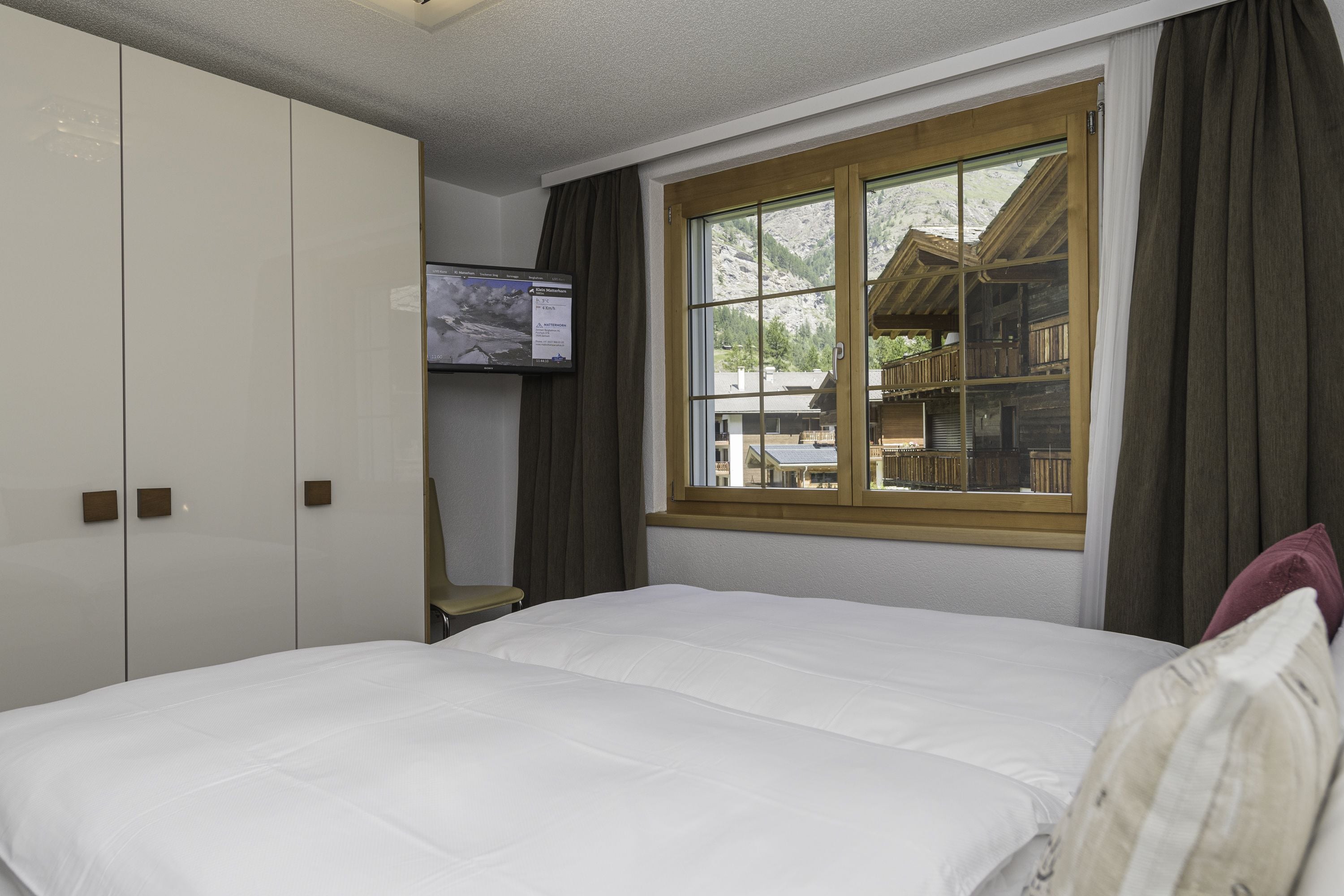 Een slaapkamer met een groot bed, een aan de muur bevestigde televisie en een raam met uitzicht op een houten hut.