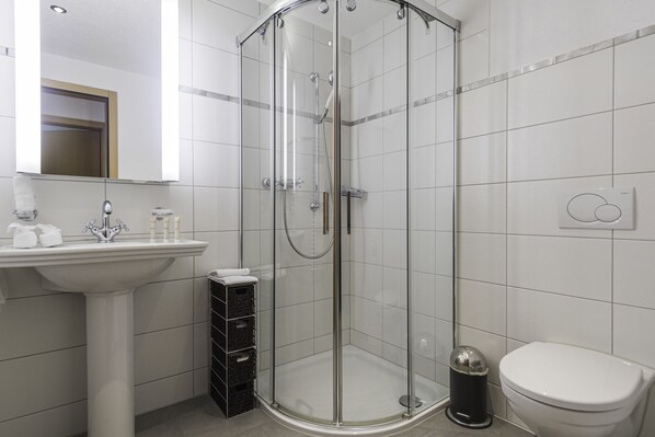 A modern bathroom with a glass-enclosed shower, a pedestal sink, and a toilet.