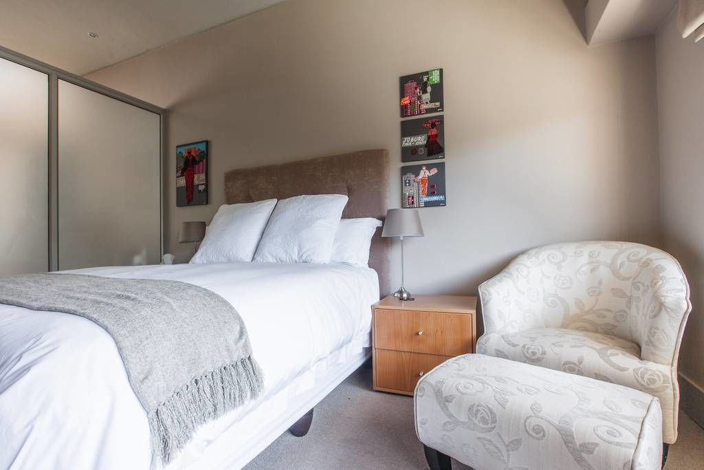 Un dormitorio con cama, mesita de noche, lámpara, silla y decoración en la pared.