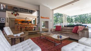 A spacious living room with a large window, a sofa, a coffee table, and a dining area with a kitchen in the background. - Houghton Place (Johannesburg)