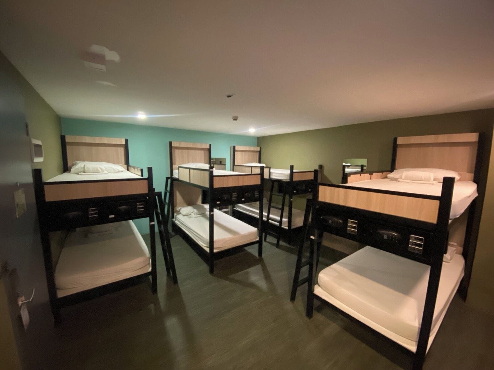 A dormitory room with bunk beds, a wooden floor, and a green wall.