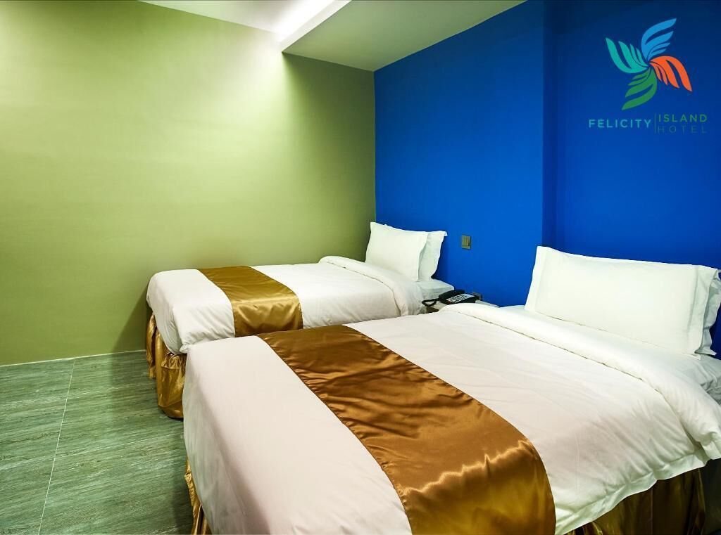 A hotel room with two beds, green and blue walls, and a logo on the blue wall.