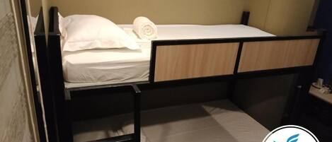 Una cama litera con escalera, un almohadón blanco y una toalla enrollada en la parte superior.