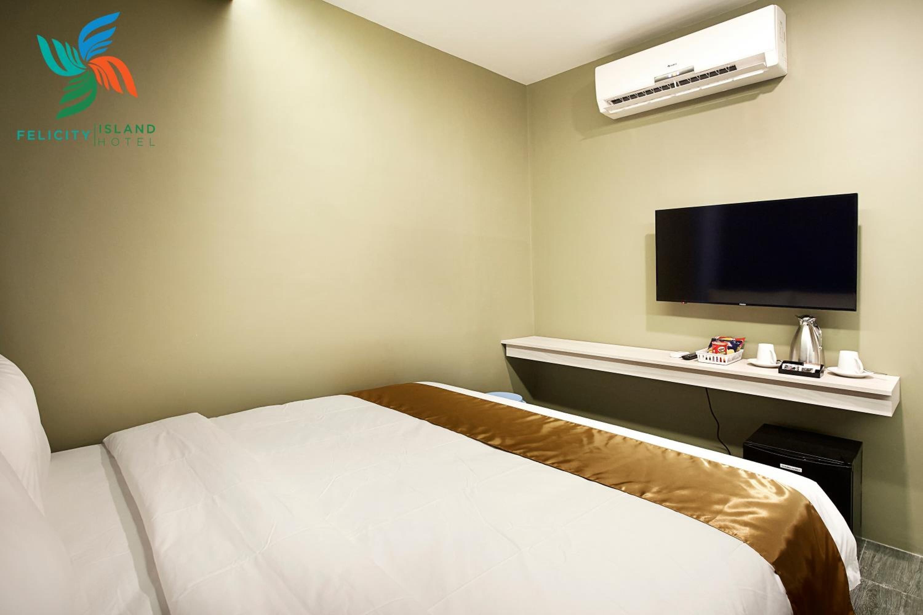 Habitación de hotel con una cama, un televisor sobre un soporte y un equipo de aire acondicionado en la pared.