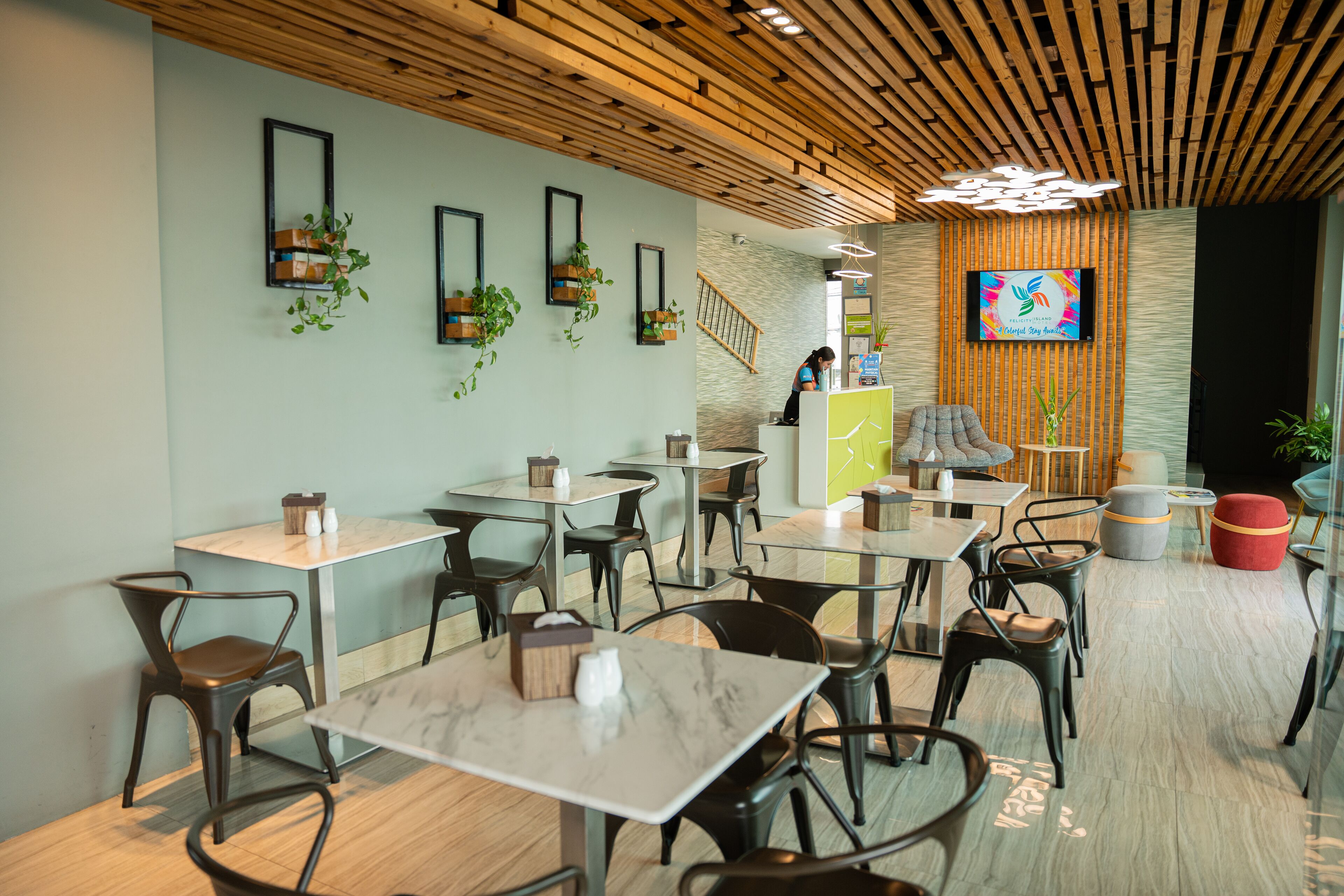 A modern cafe with wooden ceiling, black chairs, and tables.
