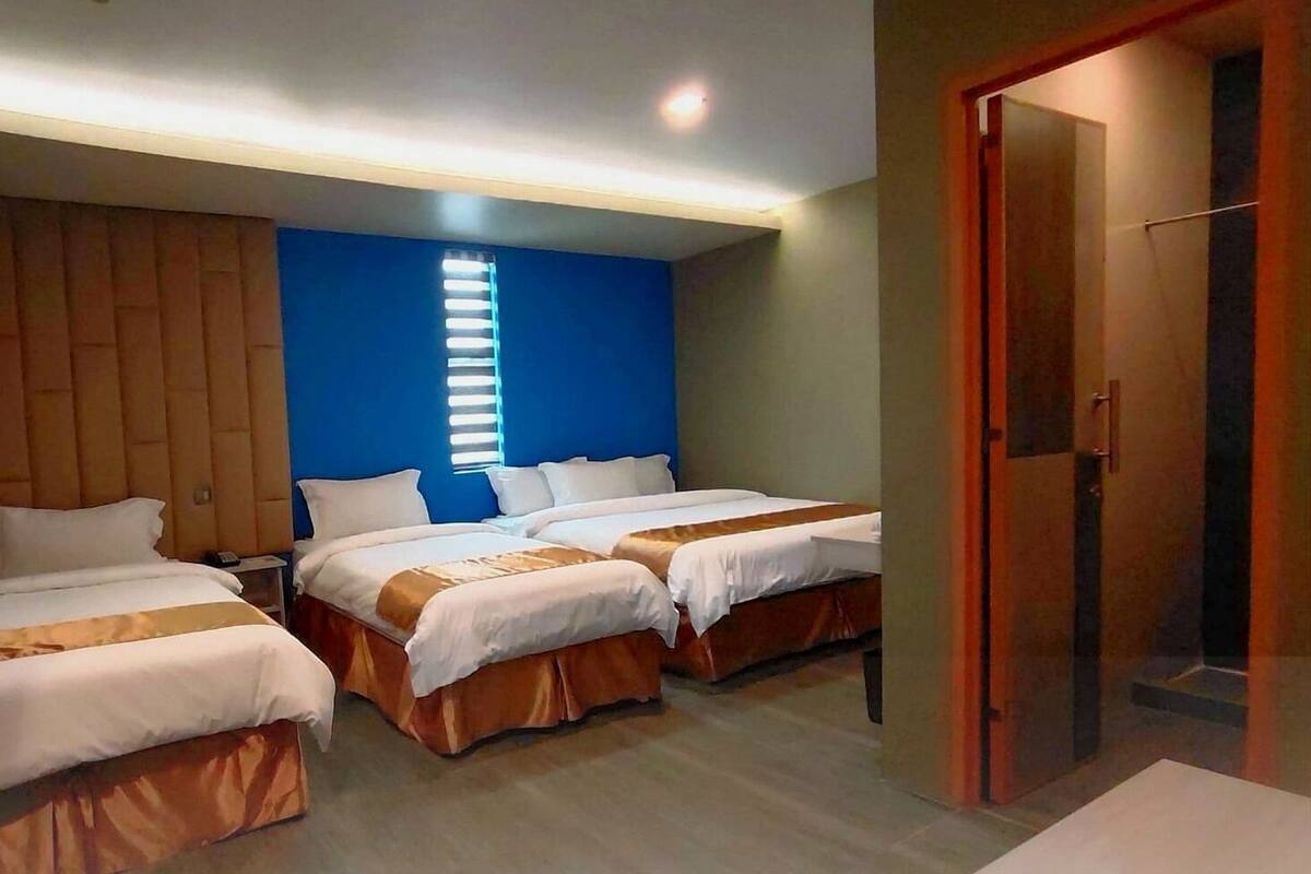 A hotel room with two beds, a wooden headboard, a blue accent wall, and a door to the right.