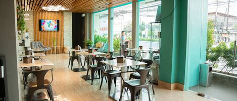 Una cafetería moderna con techo de madera, ventanas amplias y diversas opciones de asientos.