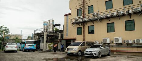 Un estacionamiento con varios autos, un edificio con múltiples unidades de aire acondicionado y un tanque de agua al fondo.