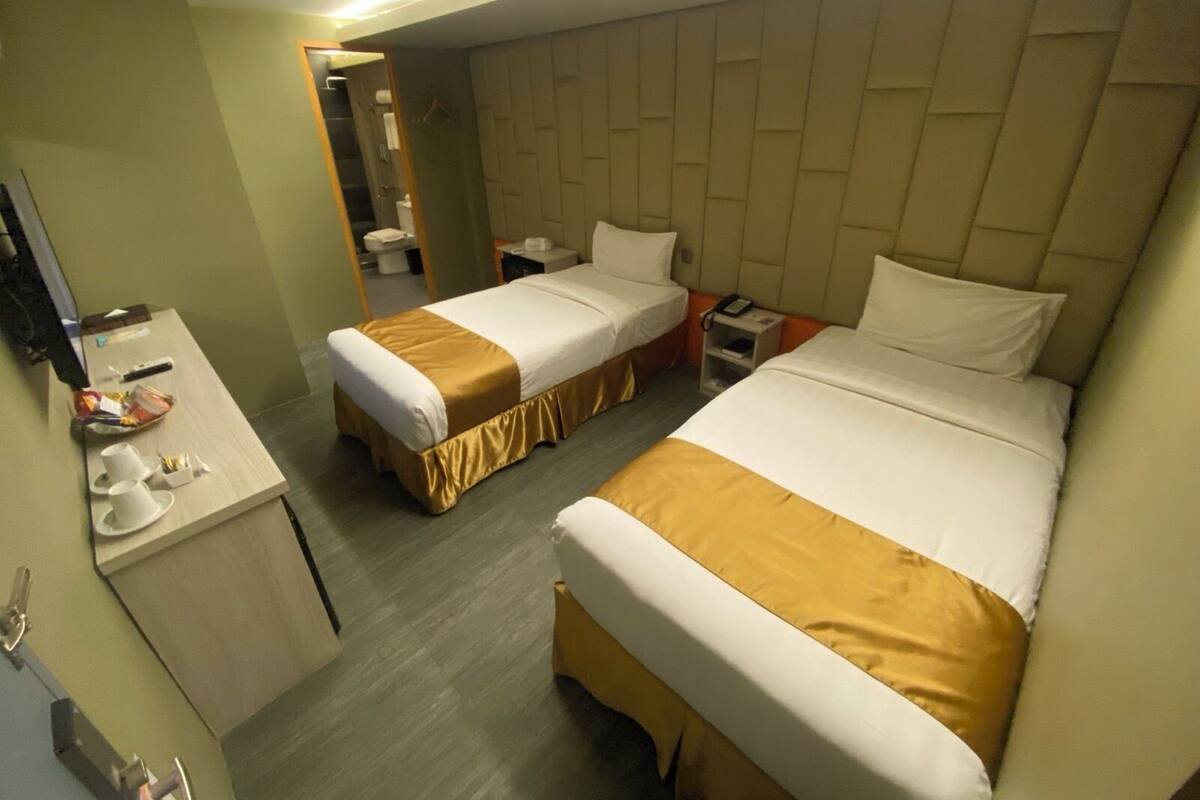 A hotel room with two single beds, a small desk with a telephone, and a mirror.