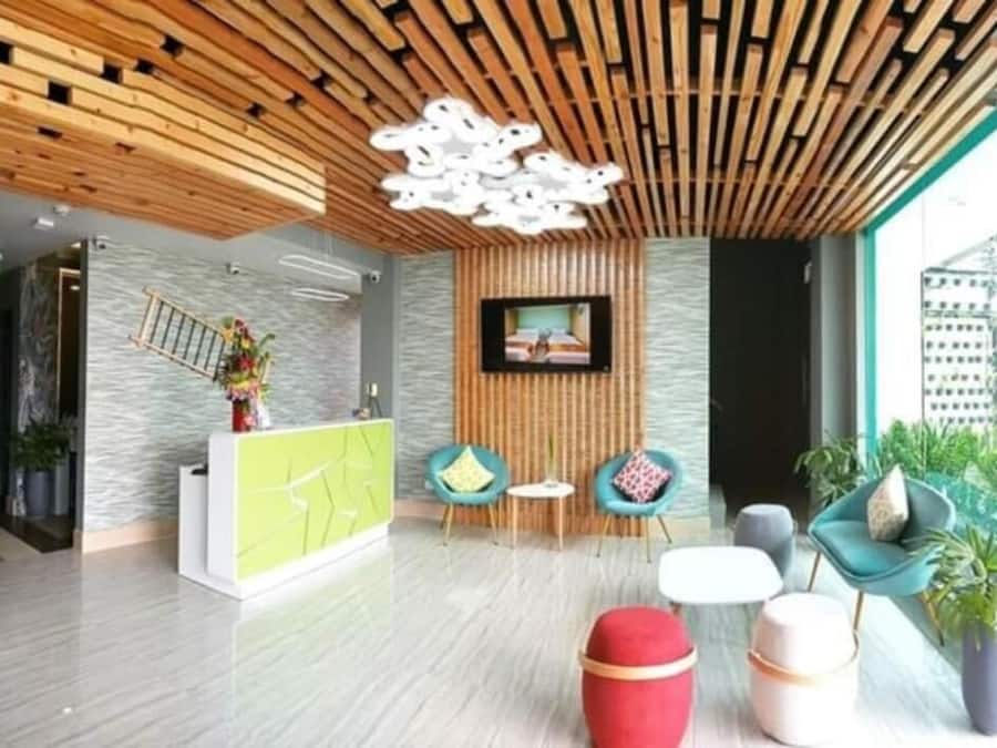 A modern reception area with a wooden ceiling, a green reception desk, two teal chairs, a red ottoman, and a television on the wall.