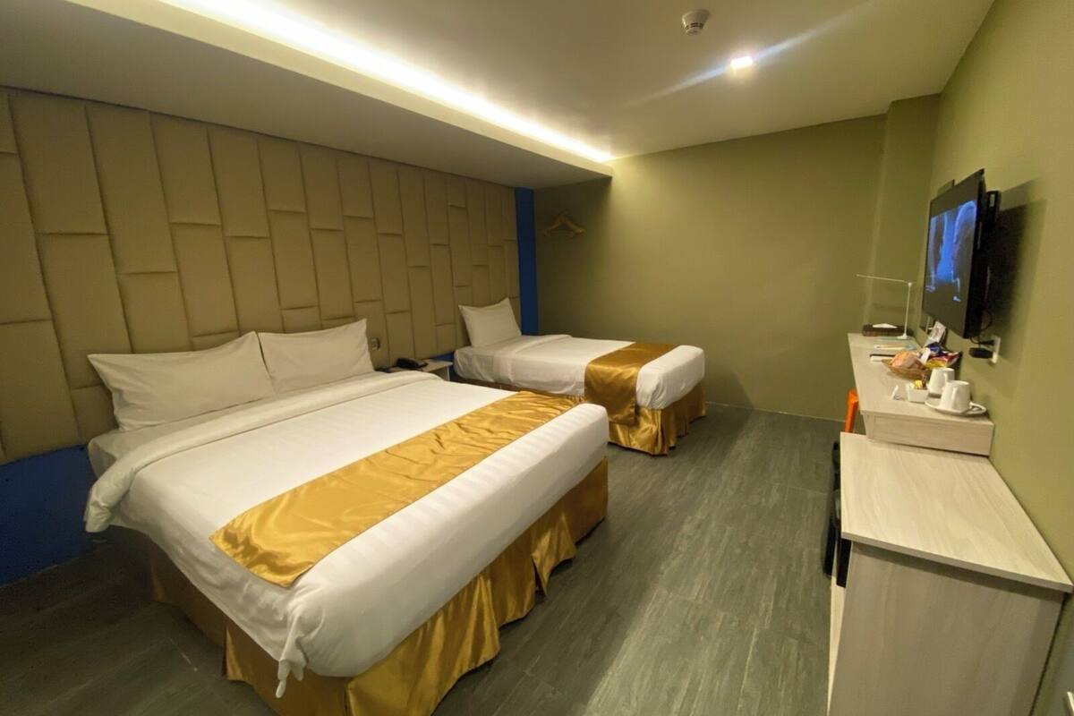 A hotel room with two beds, a desk with a TV, and a wall-mounted TV.