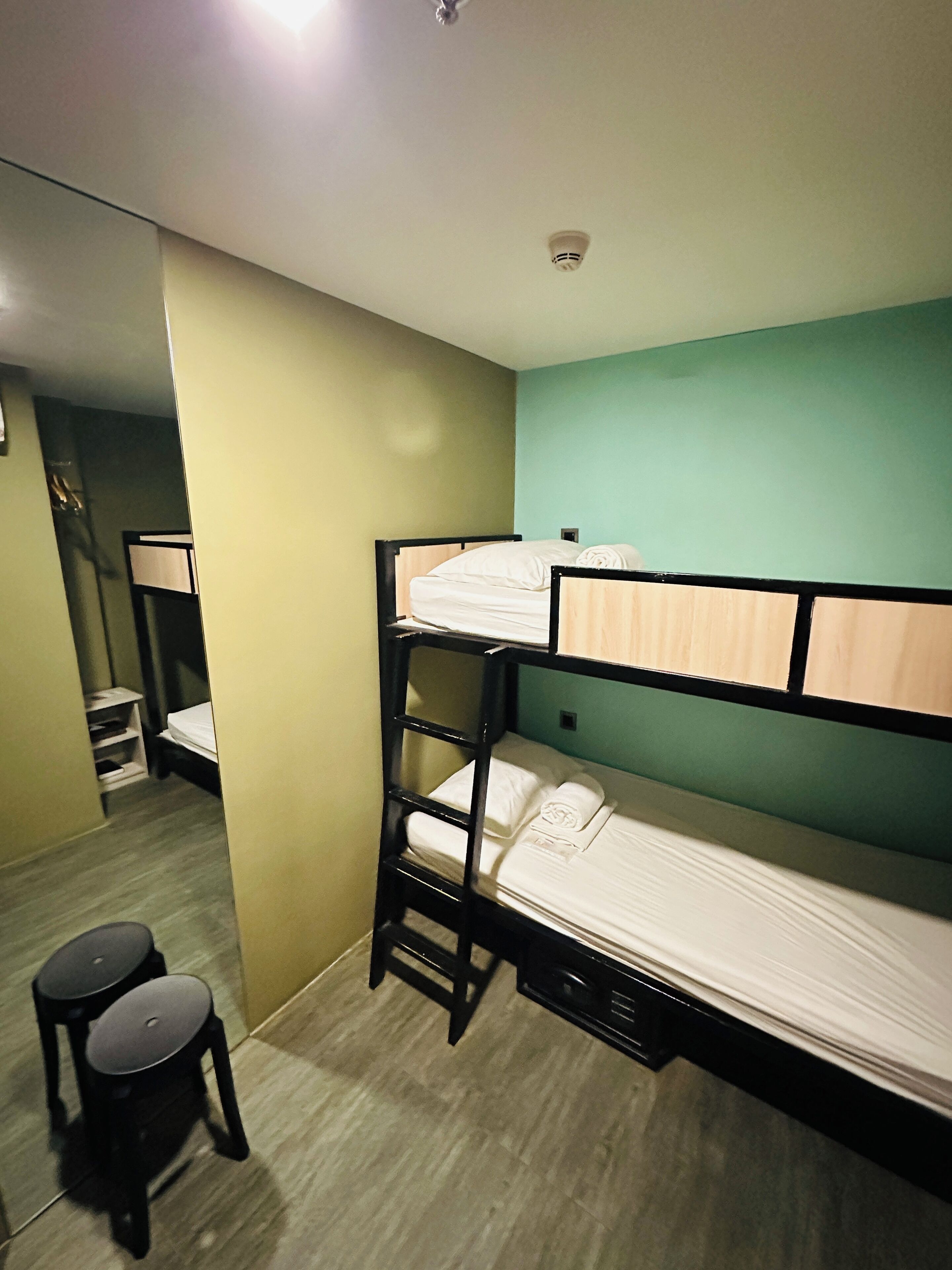 A bunk bed room with a ladder, a small stool, and a desk with a lamp.