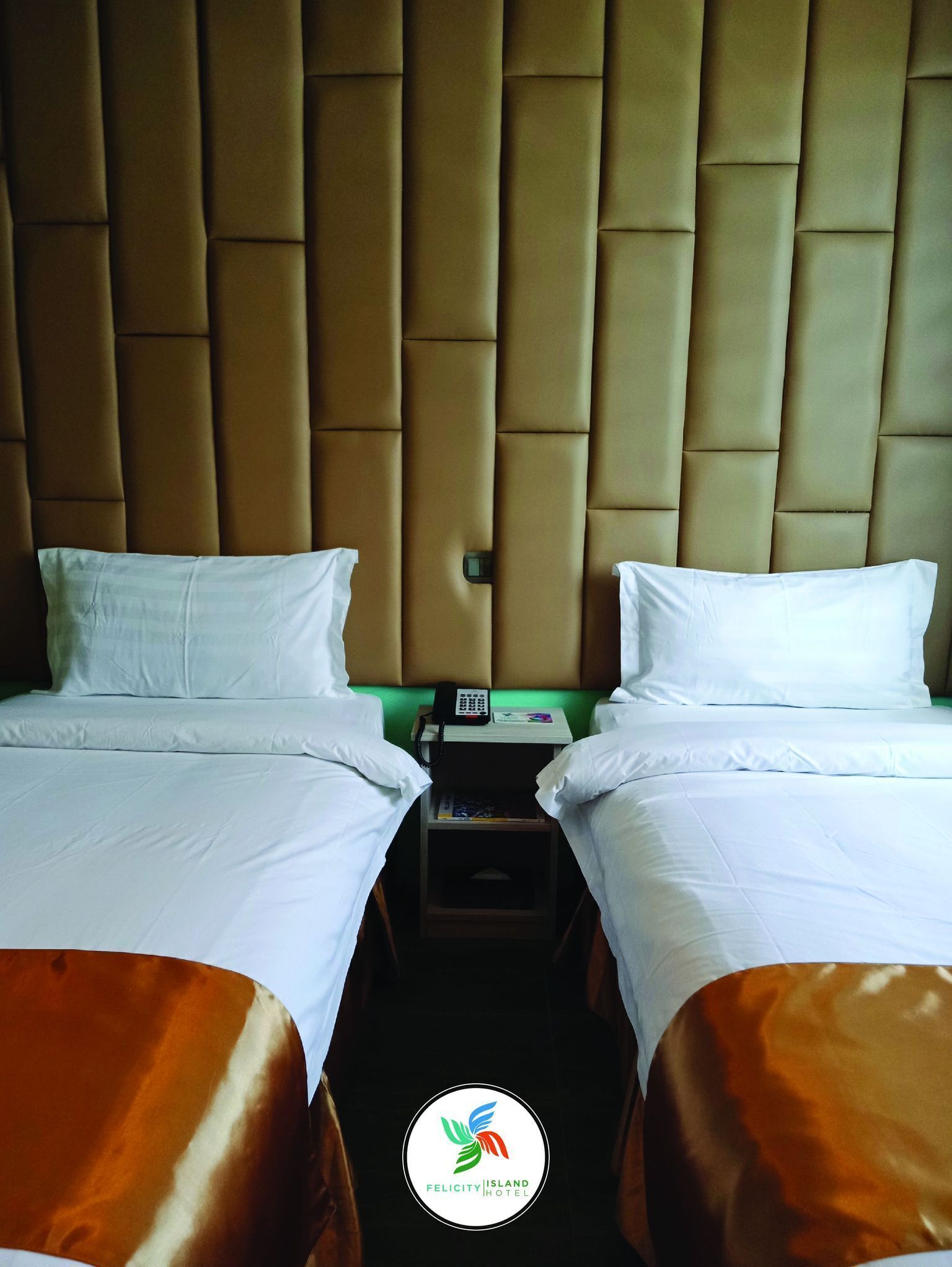A hotel room with two beds, a nightstand with a phone, and a green wall.