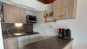 Una cocina compacta con armarios de madera, microondas integrado, cafetera y lavavajillas.