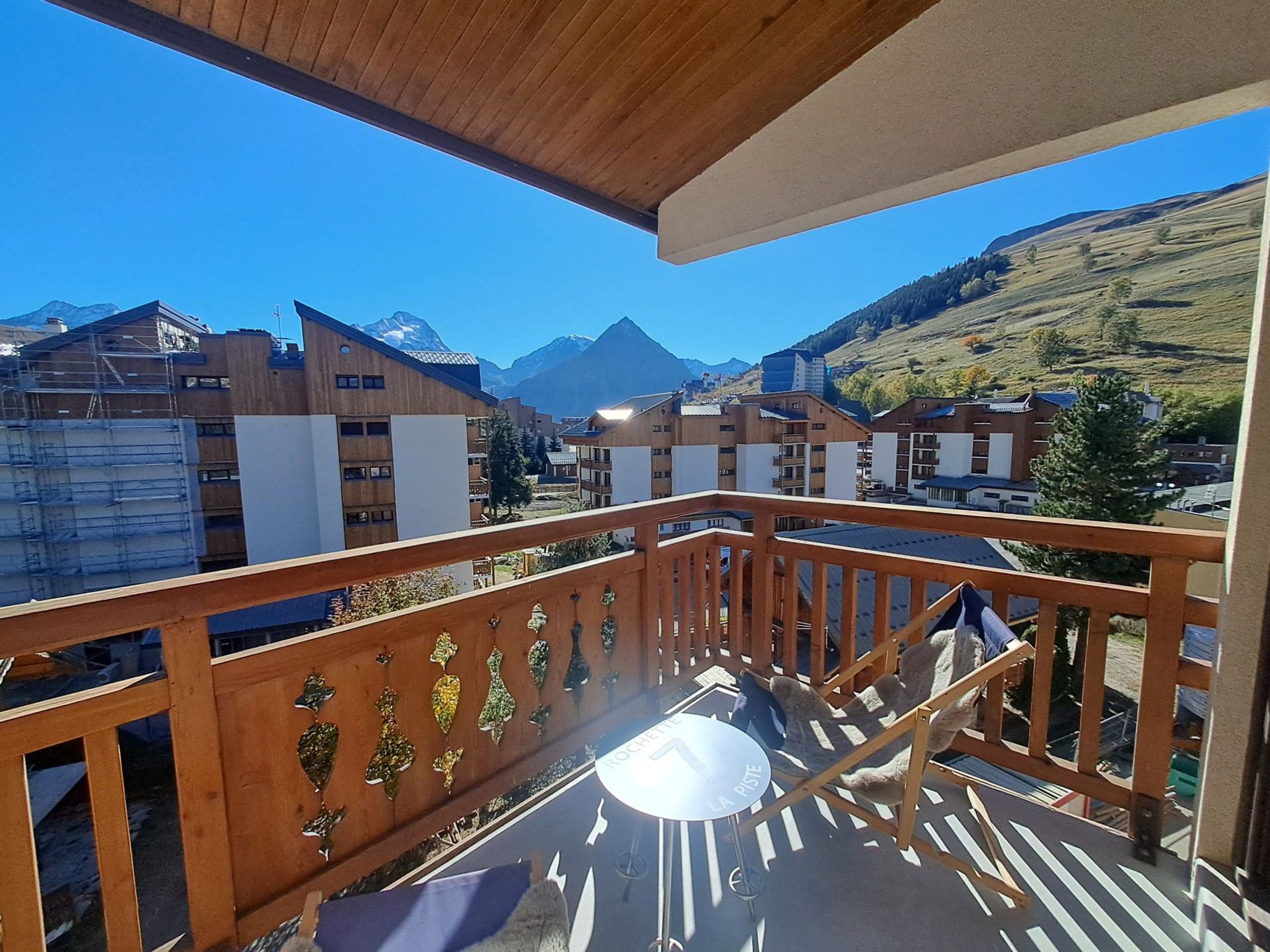Een balkon met uitzicht op een bergachtig landschap, houten leuningen en een tafel met een stoel.