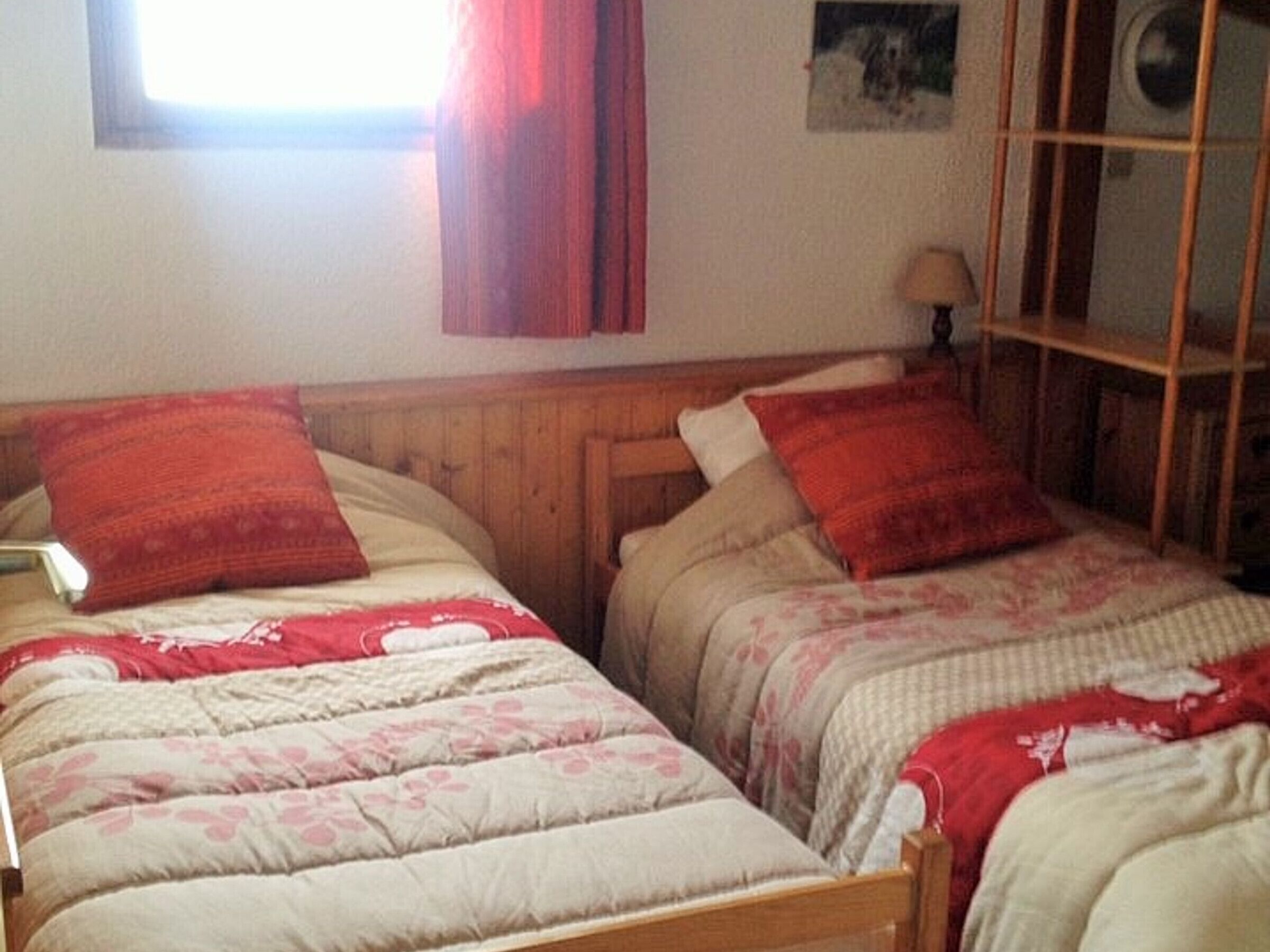 A bedroom with two beds, each with a wooden headboard and red bedding.