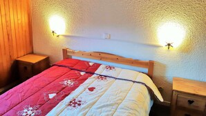 Una cama con colcha roja y blanca, cabecera de madera, dos mesitas de noche y lámparas fijadas a la pared.