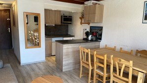 Una cocina moderna con armarios de madera, una isla central y un comedor con una mesa redonda y sillas de madera.
