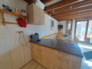 A kitchen with wooden cabinets, a countertop, a kettle, and a television.