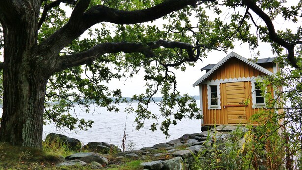 Una cabaña de madera junto a un lago, rodeada de rocas y árboles.