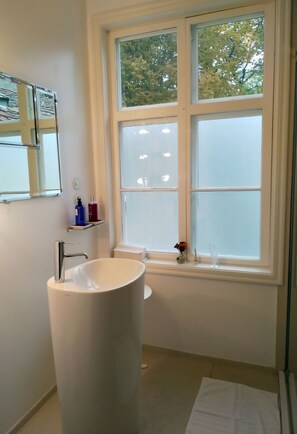 Un baño con un lavamanos grande de color blanco, un espejo y una ventana con vidrio esmerilado.