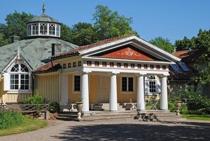 Un edificio con una entrada central flanqueada por columnas, una estructura en forma de cúpula y un tejado de tejas.