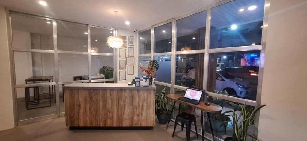 A modern reception area with a wooden reception desk, a laptop on a small table, and a view of the street through large windows.