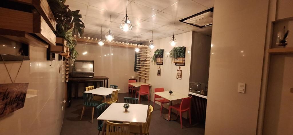 A dining area with tables and chairs, a kitchen area, and a wall-mounted shelf with plants.