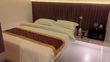 A hotel room with a bed, bedside table, lamp, and a control panel.