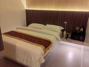 A hotel room with a bed, bedside table, lamp, and a control panel. - Kojo Hotels Tagum (Tagum)