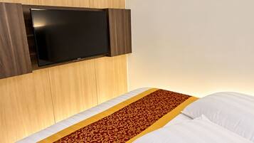 A hotel room with a bed, a flat-screen TV mounted on the wall, and a patterned bed runner.