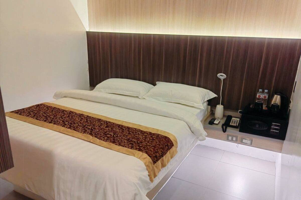 Una habitación de hotel con una cama grande, una mesita de noche con lámpara y un panel de control.
