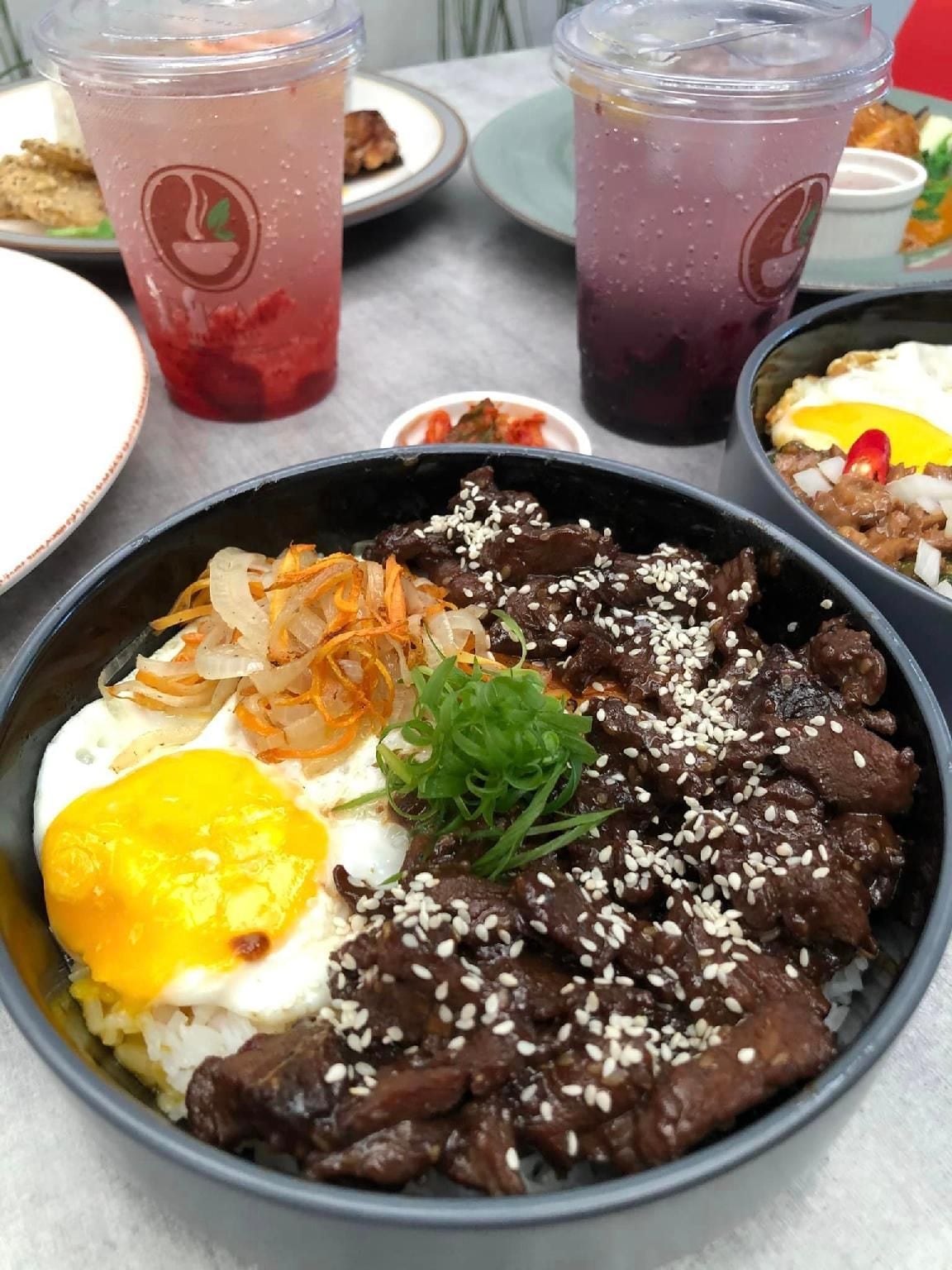 A meal with beef, rice, and a fried egg, accompanied by two drinks.