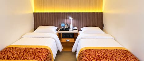 A hotel room with two single beds, a bedside table with a lamp, a coffee maker, and a phone.