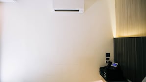 A room with a white air conditioning unit on the wall, a black electronic device on a stand, and a dark-colored headboard.